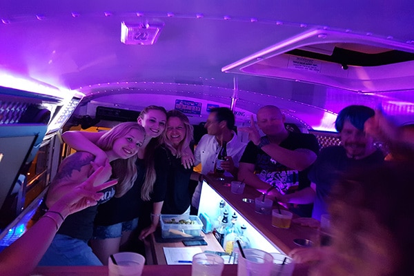 8 Personen feiern und lachen an der Bar im Partybus bei lila Partylicht