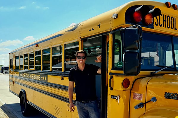 Busfahrer in der Tür von einem gelben US Schoolbus Partybus